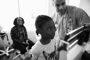 Male nurse checking weight of girl on scale in clinic examination room