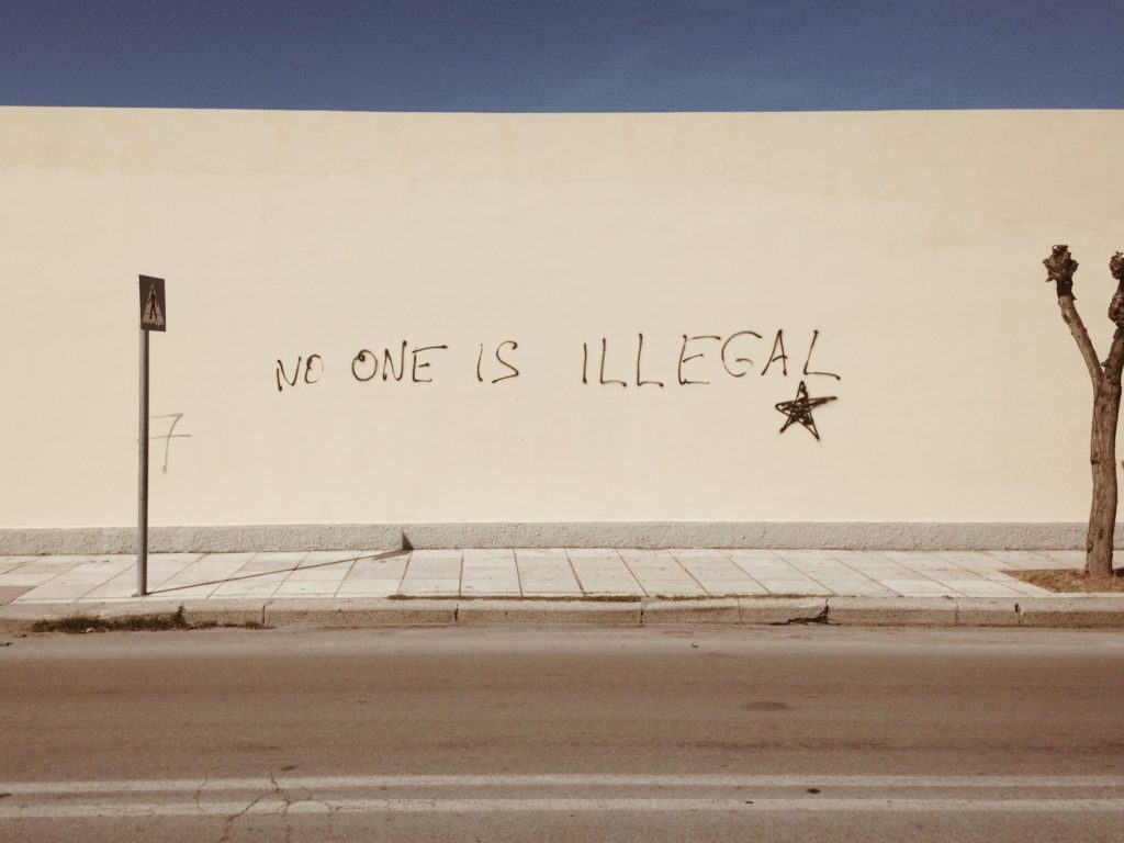 A wall spray-painted with the words "no one is illegal."
