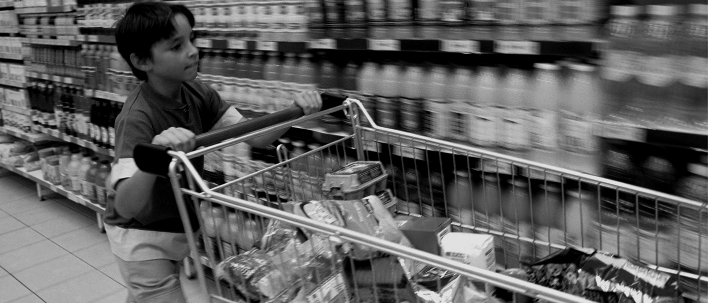 young boy pushing shopping cart down food aisle
