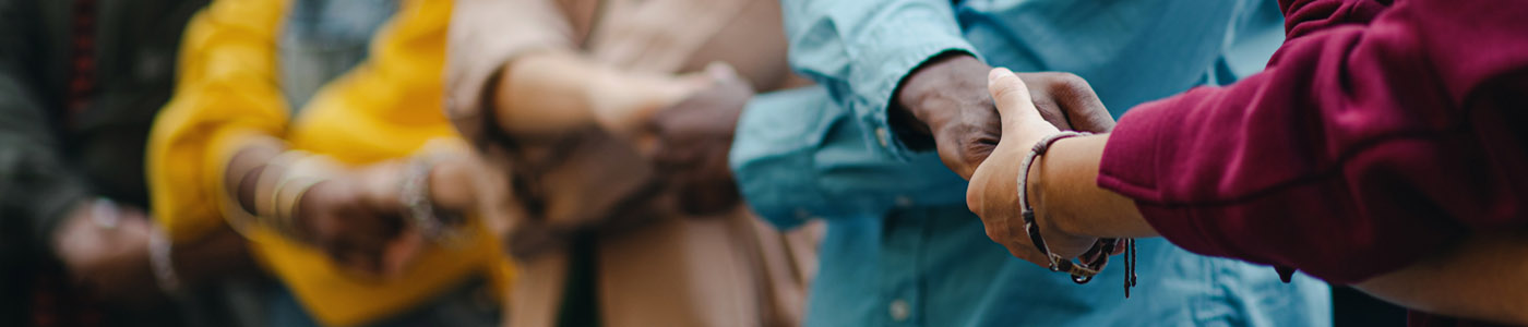 Row of multicultural people lined up, holding hands, with arms crossed over arms.
